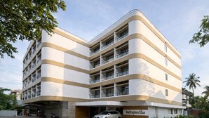 A multi-story hotel with a modern design, featuring a curved facade and a parking area in front. - Hotel Indraprastha (Palakkad)