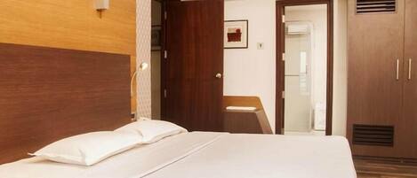 Habitación de hotel con cama, cabecera de madera, armario y un escritorio pequeño con silla.