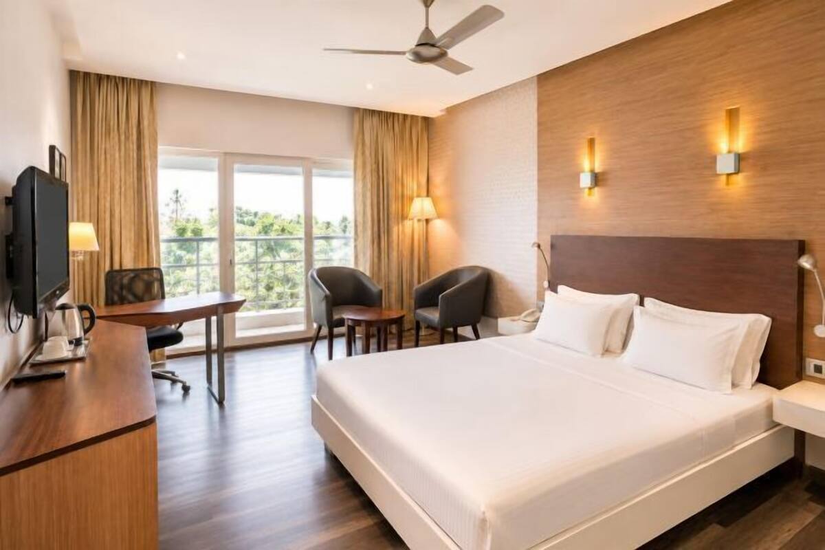 A hotel room with a bed, desk, chairs, a television, and a balcony.