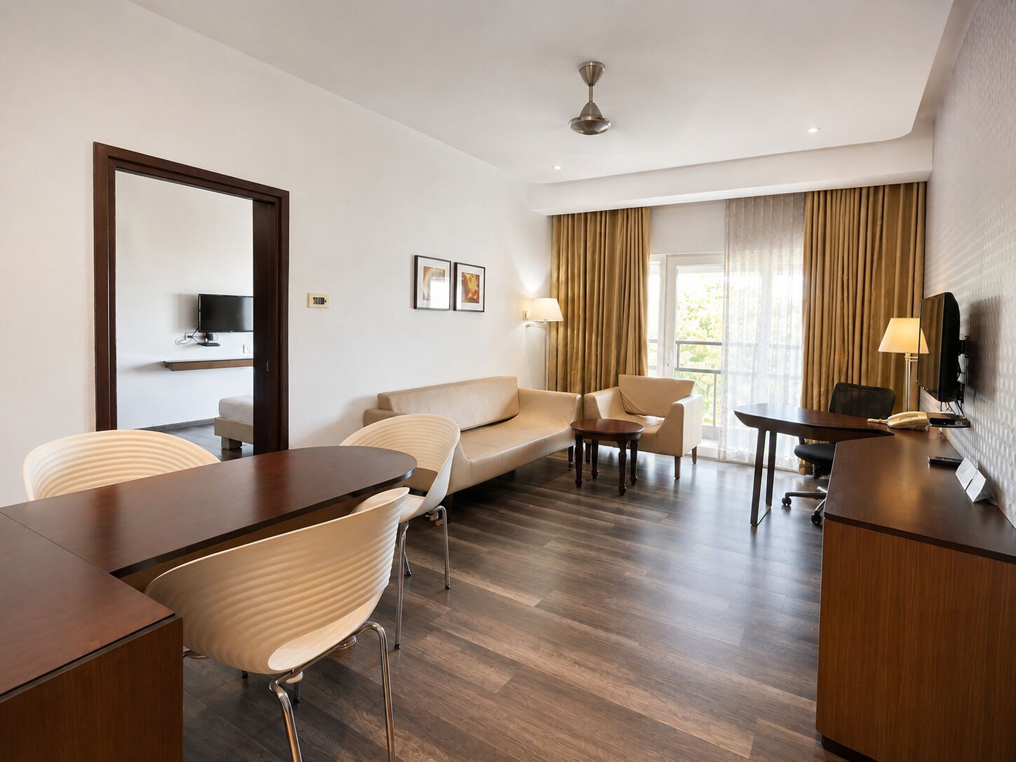 A hotel room with a sofa, chairs, a desk, a television, and a large window with curtains.
