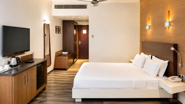 A modern hotel room with a large bed, a flat-screen TV, a desk with a coffee maker, and a ceiling fan. - Hotel Indraprastha (Palakkad)