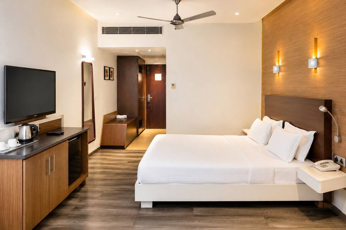 A modern hotel room with a large bed, a flat-screen TV, a desk with a coffee maker, and a ceiling fan.