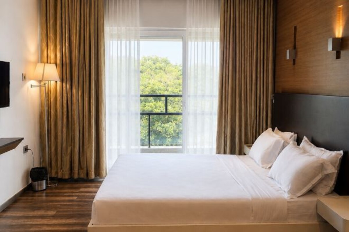 Habitación de hotel con una cama grande, un televisor en la pared y una ventana con cortinas.