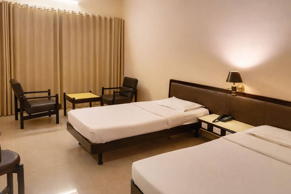 A hotel room with two beds, a desk, two chairs, a lamp, and a telephone.