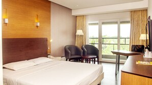 A hotel room with a bed, two chairs, a desk, and a large window with a view. - Hotel Indraprastha (Palakkad)