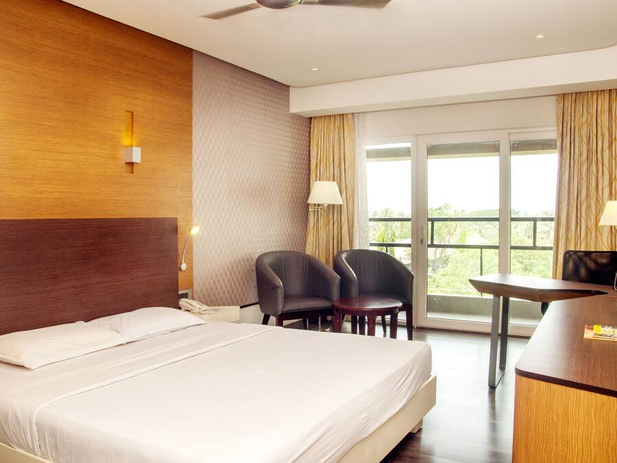Habitación de hotel con cama, dos sillas, escritorio y un gran ventanal con vistas.
