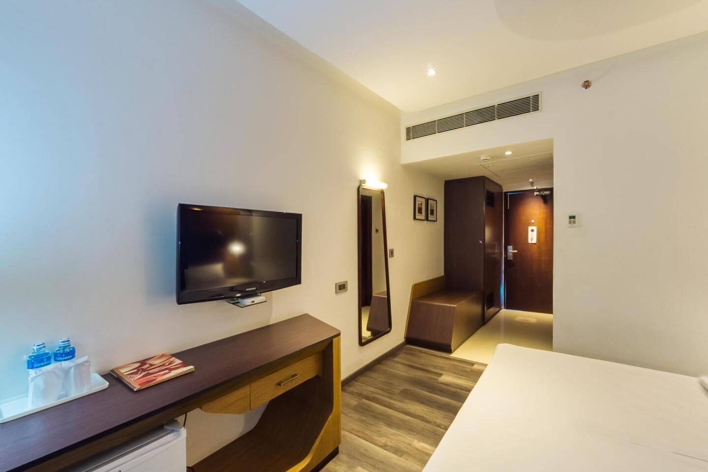 Una habitación de hotel con una televisión de pantalla plana, un escritorio de madera, una cama y un espejo.