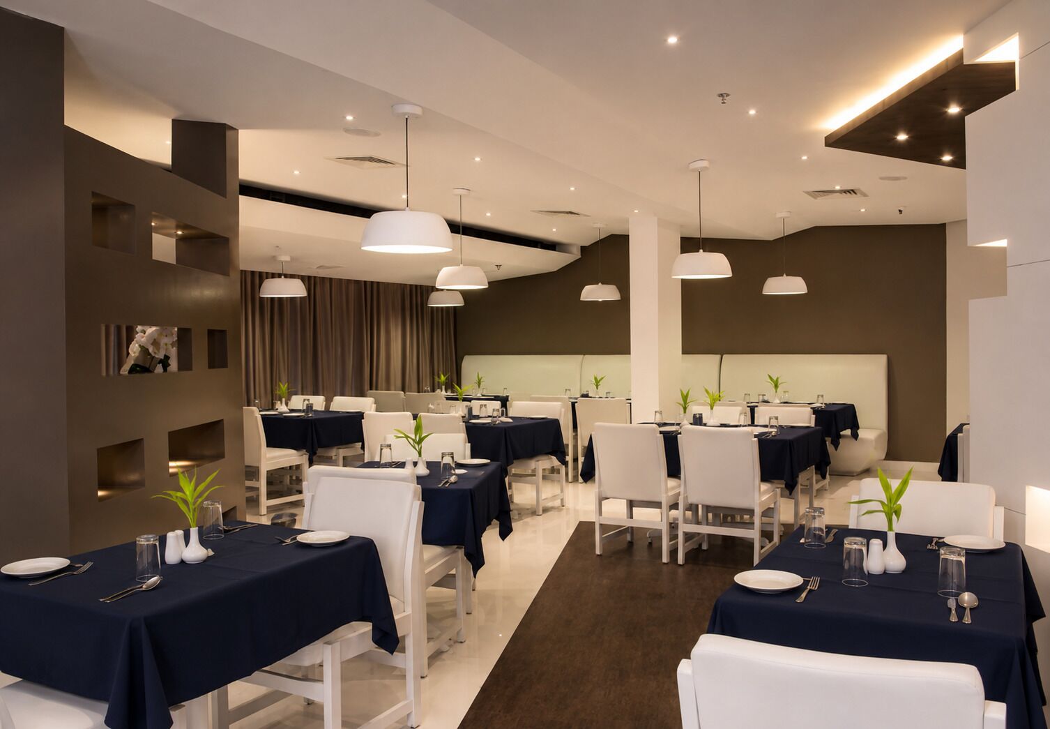 Un espace de restauration moderne avec plusieurs tables, des chaises blanches et des luminaires suspendus.