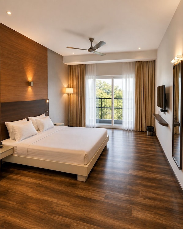 A modern hotel room with a large bed, a ceiling fan, a TV, and a view of greenery through the window. - Hotel Indraprastha (Palakkad)