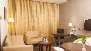 A hotel room with a sofa, a small table with a coffee pot, a desk, and a TV mounted on the wall. - Hotel Indraprastha (Palakkad)