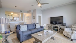 A living room with a grey sofa, a coffee table, a TV, and a striped armchair. - Waterfront 2BR Townhome w/ 4 Balconies, Views of River, Bay & St. Pete – Near Beach & Pool (Ruskin)
