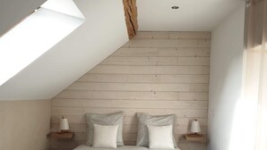 Ein Schlafzimmer mit schräg versiegelter Decke, einem Bett mit gemustertem Überwurf, zwei Nachttischlampen und einem Holz-Kopfteil.