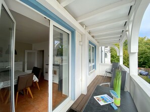 A covered balcony with a dining area, a table with a magazine, and a chair. - OS: Haus Holstein Whg. 11 mit Balkon - Haus Holstein Whg. 11 mit Balkon (Sellin)