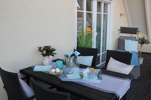Un área de estar al aire libre con una mesa dispuesta para dos personas, con un jarrón de flores, una vela y una bandeja con vasos y un postre.