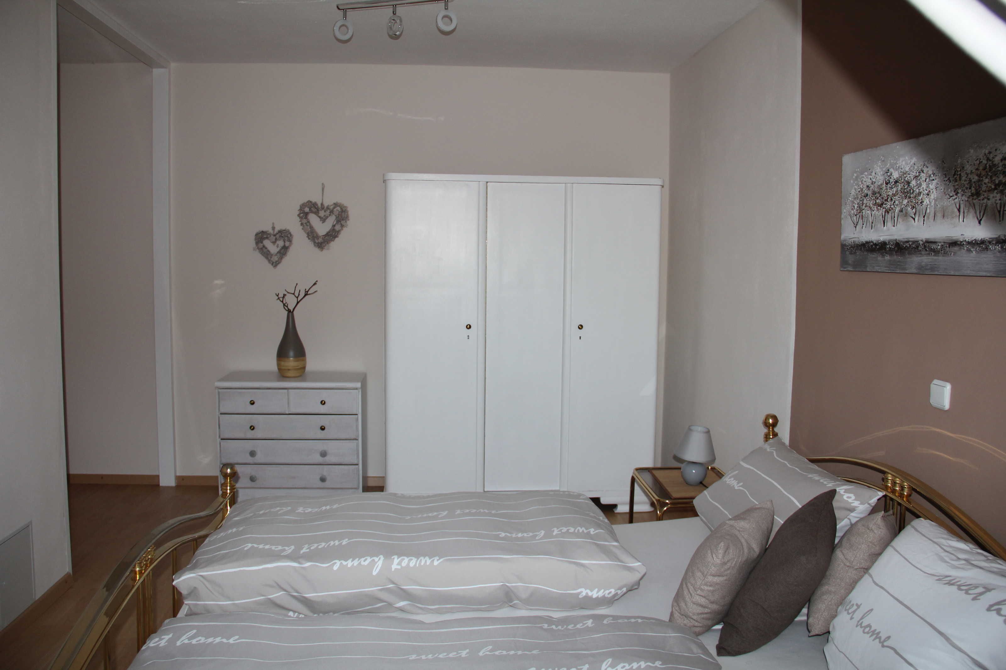 Un dormitorio con cama, cómoda, armario, mesita de noche y lámpara.