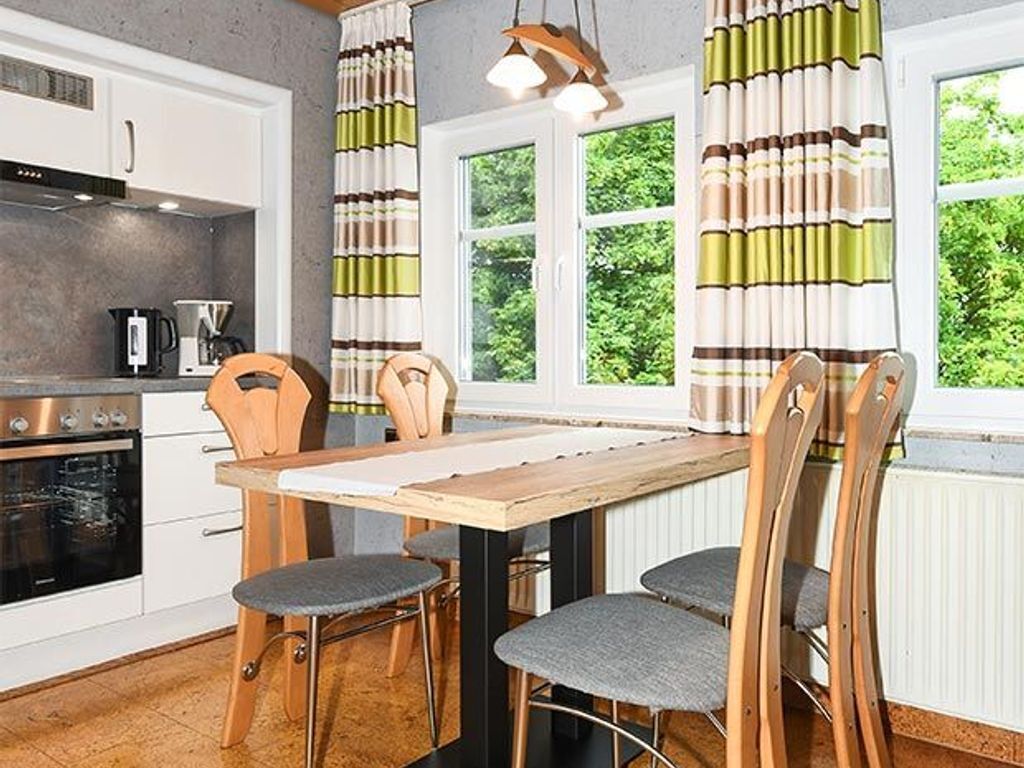 A kitchen with a wooden table and chairs, a stove, and a window with curtains.