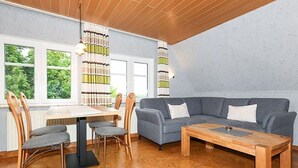 Ein modernes Wohnzimmer mit Essbereich, ausgestattet mit einem grauen Sofa, einem Holztisch und einem Esstisch mit Stühlen.