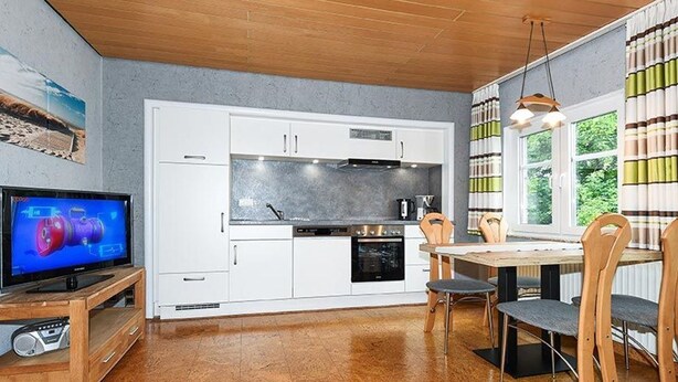Eine moderne Küche mit weißen Schränken, einem eingebauten Backofen und einem Essbereich mit Holztisch und Stühlen.