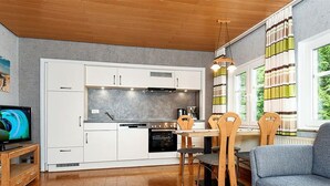 Eine moderne Küche mit weißen Schränken, eine Essecke mit Holztisch und -stühlen sowie ein Wohnzimmer mit blauem Sofa.