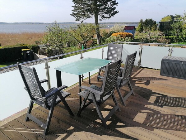 Une terrasse dotée d’une table et de chaises en verre, avec vue sur un lac.