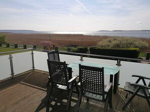 Une terrasse avec deux chaises et une table, offrant une vue sur une étendue d’eau et sur la terre ferme au loin.