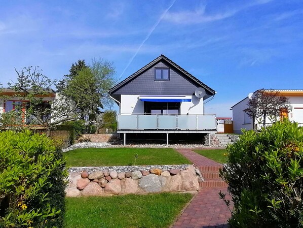 Une maison moderne à deux étages, dotée d’une antenne parabolique, d’un garage et d’un jardin bien entretenu, agrémenté d’une bordure en pierre et d’un chemin en briques.