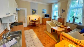 Un espacio habitable compacto con cocina, comedor y zona de estar. Incluye un lavamanos, una mesa de comedor con sillas, un sofá y un televisor.
