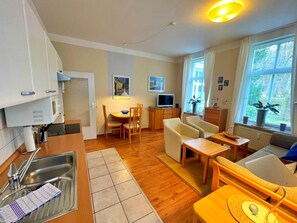 A compact living space with a kitchen, dining area, and seating area. It includes a sink, a dining table with chairs, a sofa, and a TV. - Villa Waldstraße 03 - Ferienwohnung 03 (Heringsdorf)