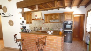 A kitchen with a brick island, two bar stools, wooden cabinets, a microwave, and a refrigerator.