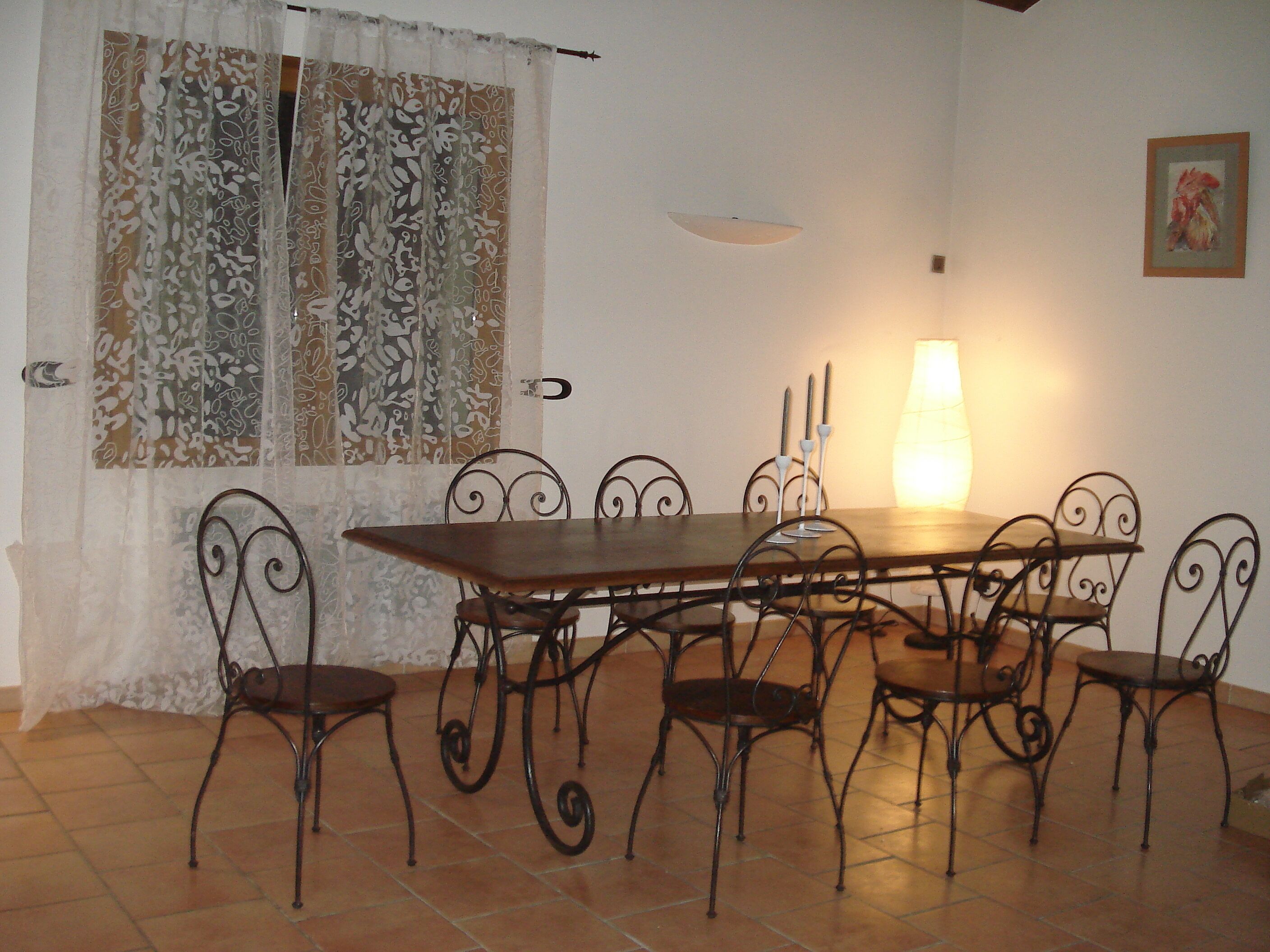 Un coin repas avec une table en bois et des chaises en métal, une fenêtre agrémentée de rideaux à motifs et une lampe fixée au mur.