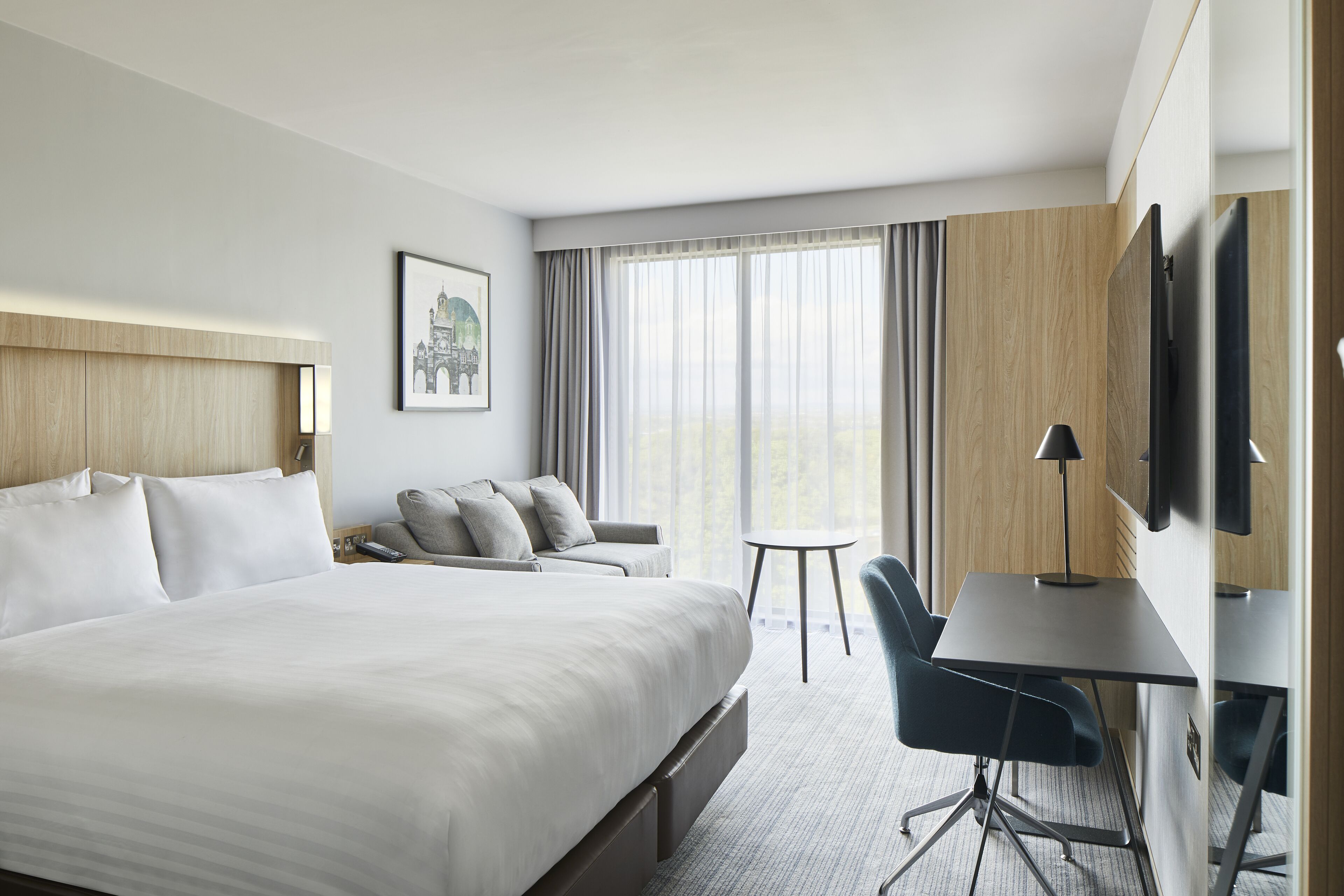 Habitación de hotel con una cama grande, un escritorio, una silla, un televisor y una ventana con cortinas.