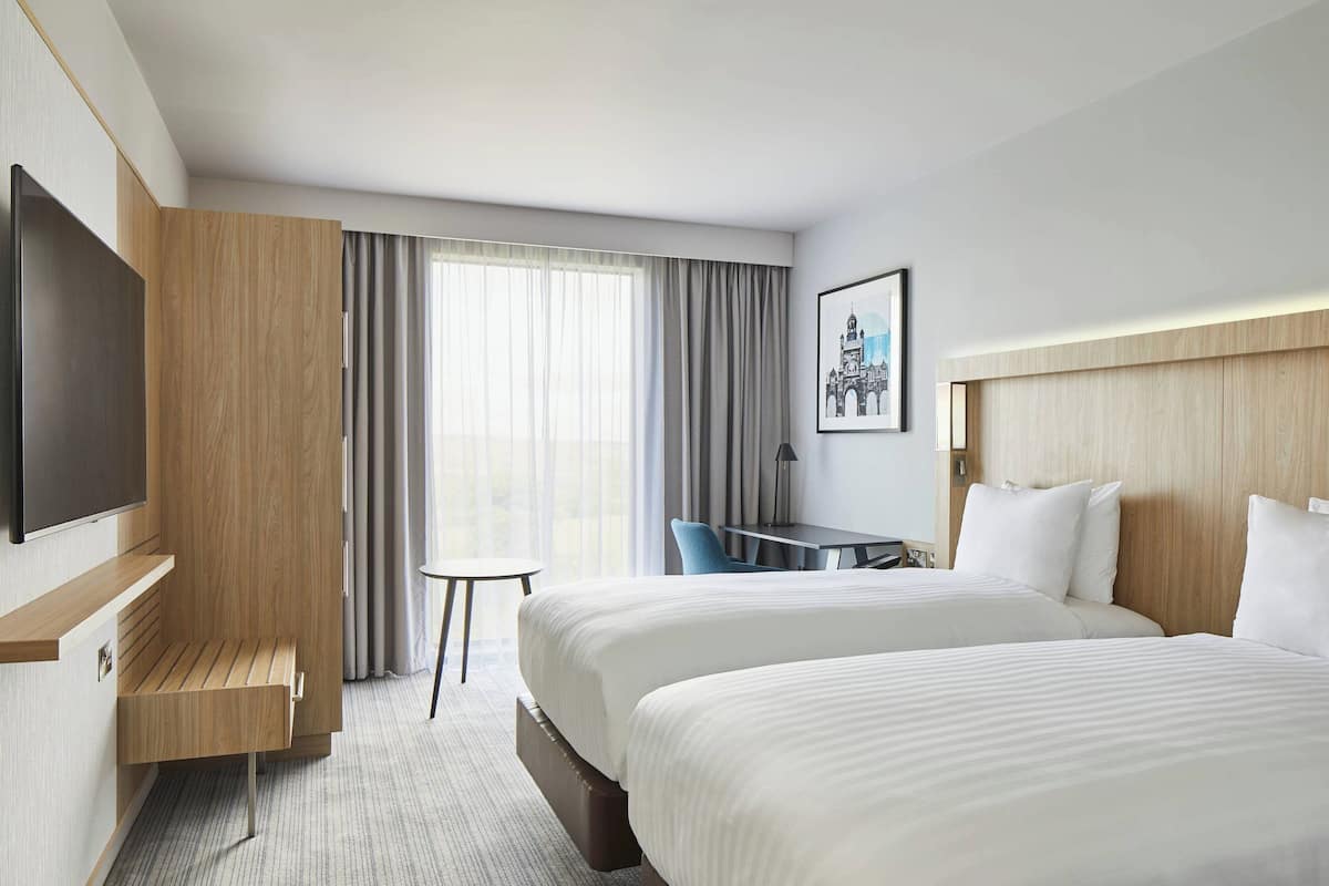 Habitación de hotel con una cama grande, un escritorio, una silla, un televisor y una ventana con cortinas.