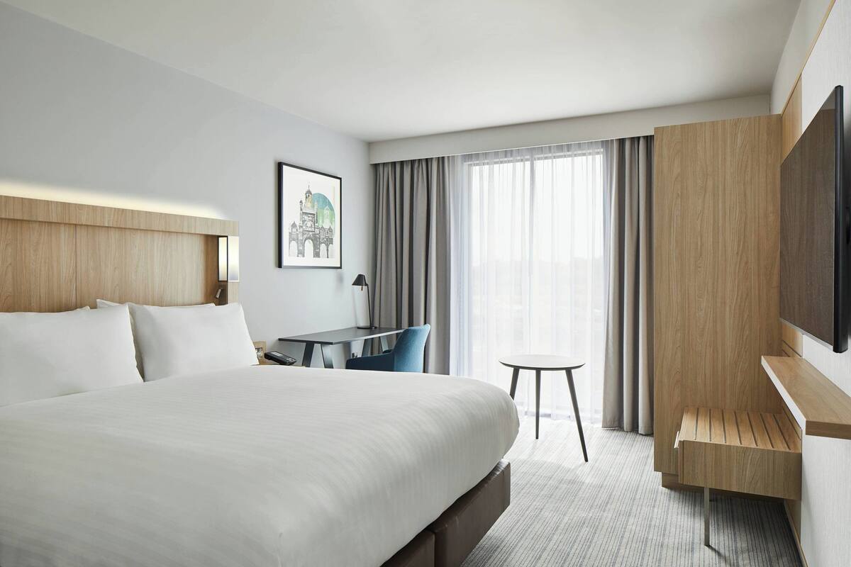 Una habitación de hotel moderna con una cama grande, un escritorio, una silla, un televisor y una ventana con cortinas.