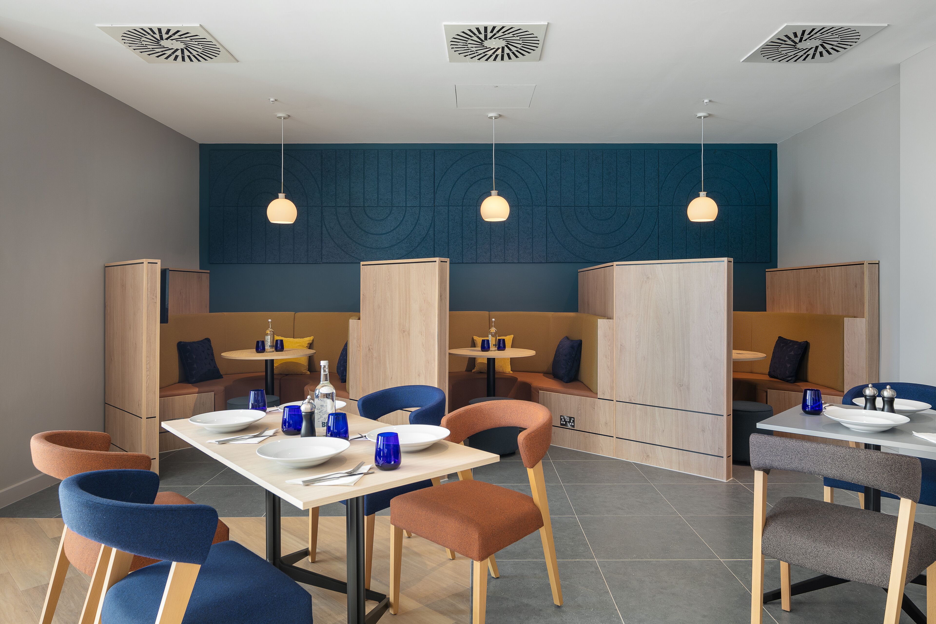 Un comedor moderno con mobiliario de madera, sillas azules e iluminación colgante.