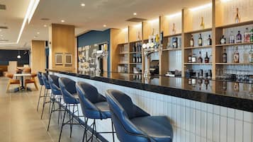 A bar area with a long counter, multiple stools, and shelves stocked with various bottles and glasses.
