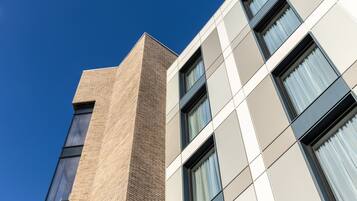 A modern building with a mix of brick and panel exteriors, large windows, and a clear blue sky.