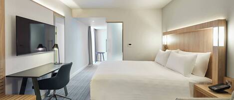 Una habitación de hotel con cama, escritorio, silla, televisor y mesita de noche.