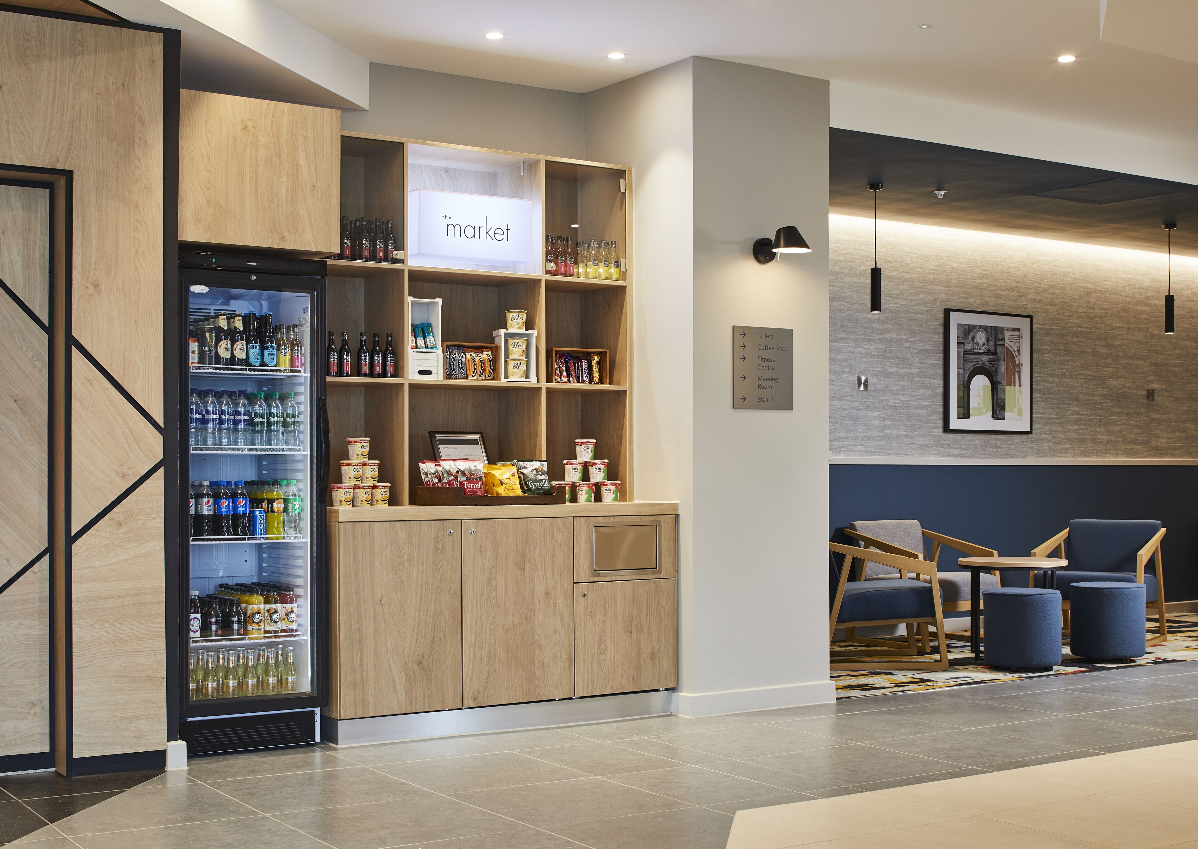 Een moderne hotellobby met een gekoeld drankendisplay, een koffiebar en een zithoek.