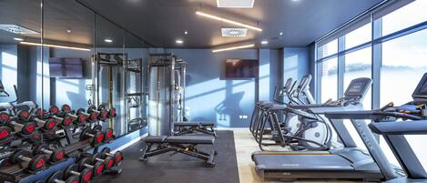 A modern gym with cardio equipment, weight machines, and dumbbells.