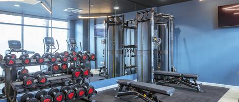 Un gimnasio con equipamiento de levantamiento de pesas, cintas de correr y una banca.