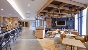 Un vestíbulo de hotel moderno con una zona de bar, asientos y un mostrador de recepción.