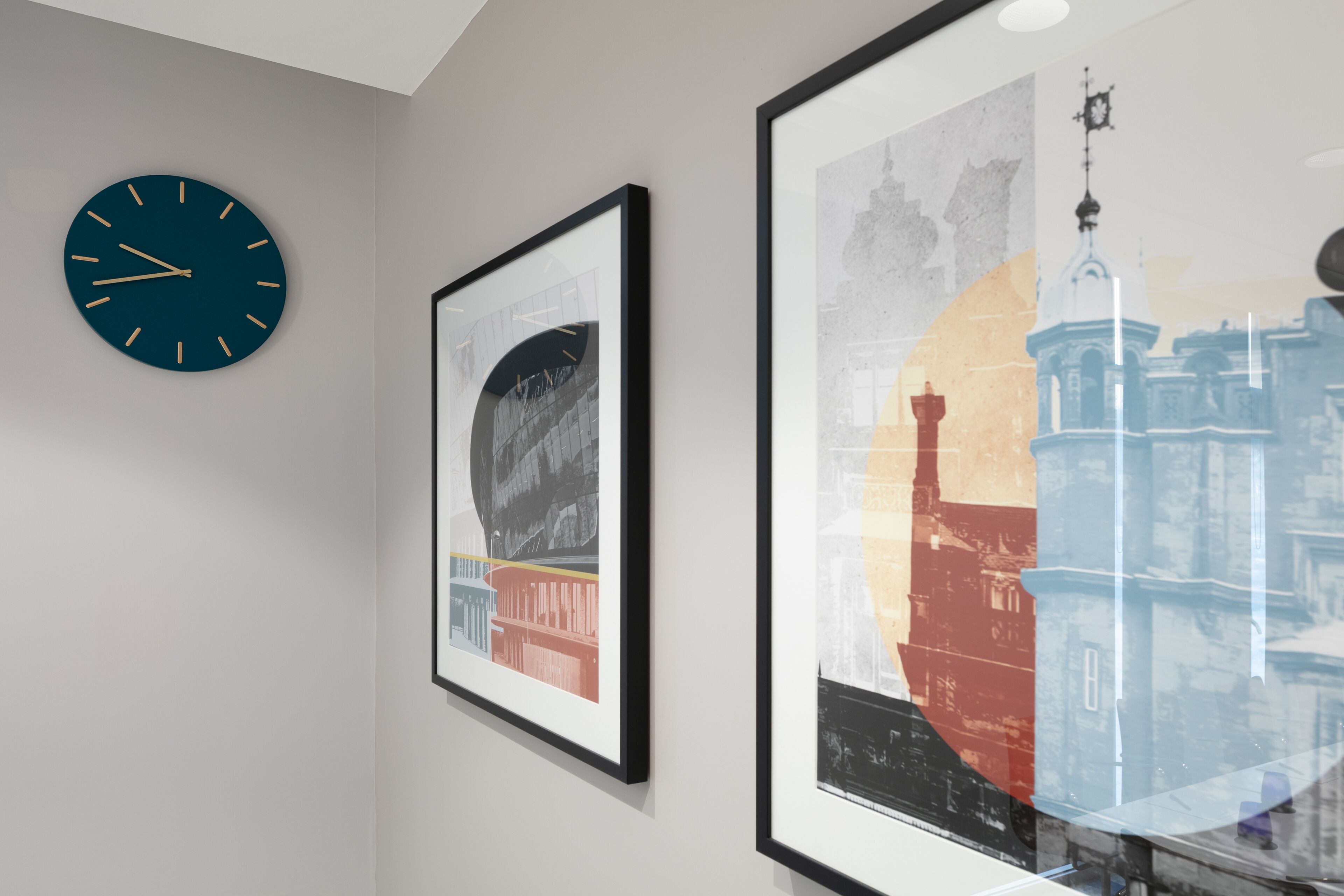 Una pared con un reloj y dos cuadros enmarcados.