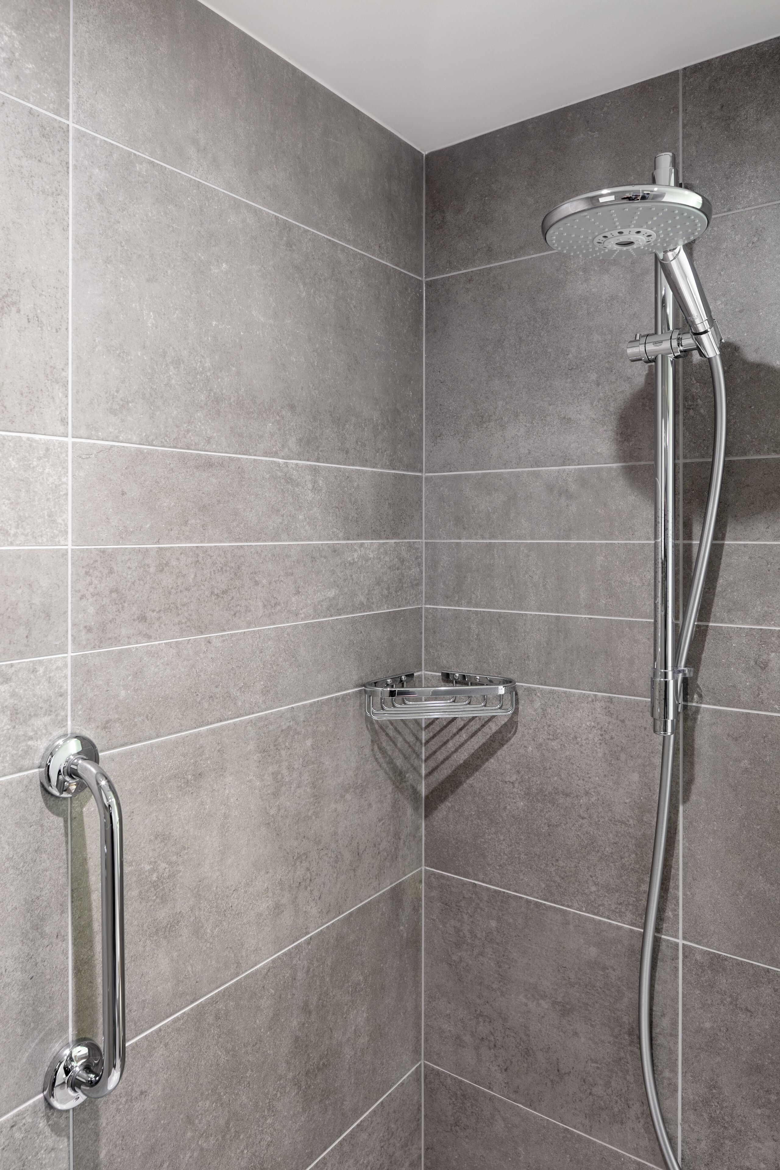 A shower area with a handheld showerhead, a handheld shower bar, and a corner sink with a soap dish.