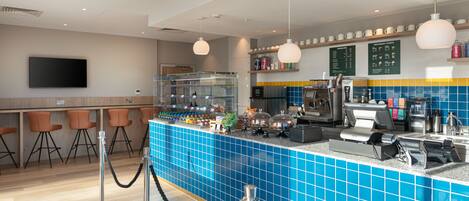 A modern bar area with blue-tiled counters, a flat-screen TV, and orange bar stools.