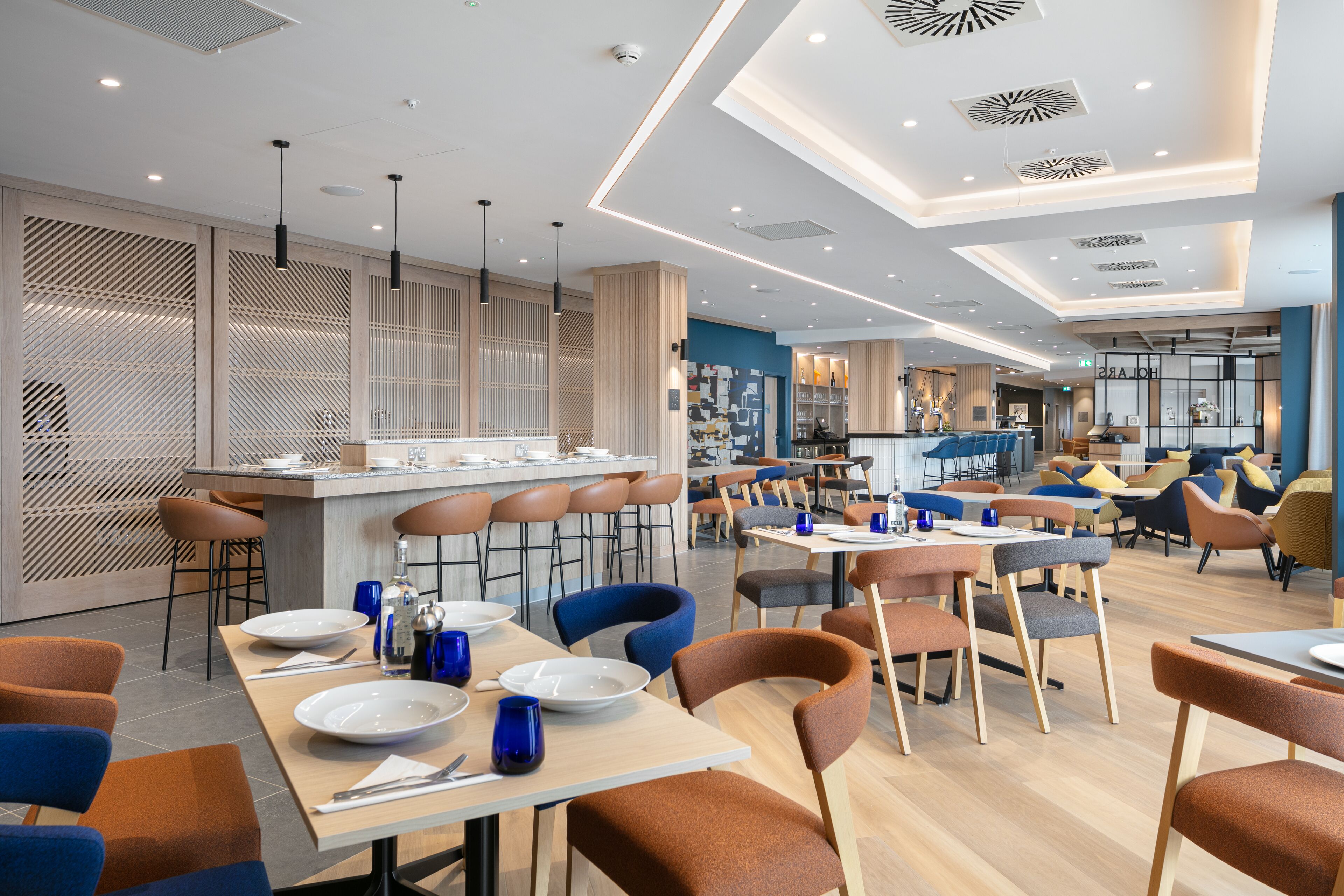 A modern restaurant with multiple dining areas, bar stools, and a central bar area.