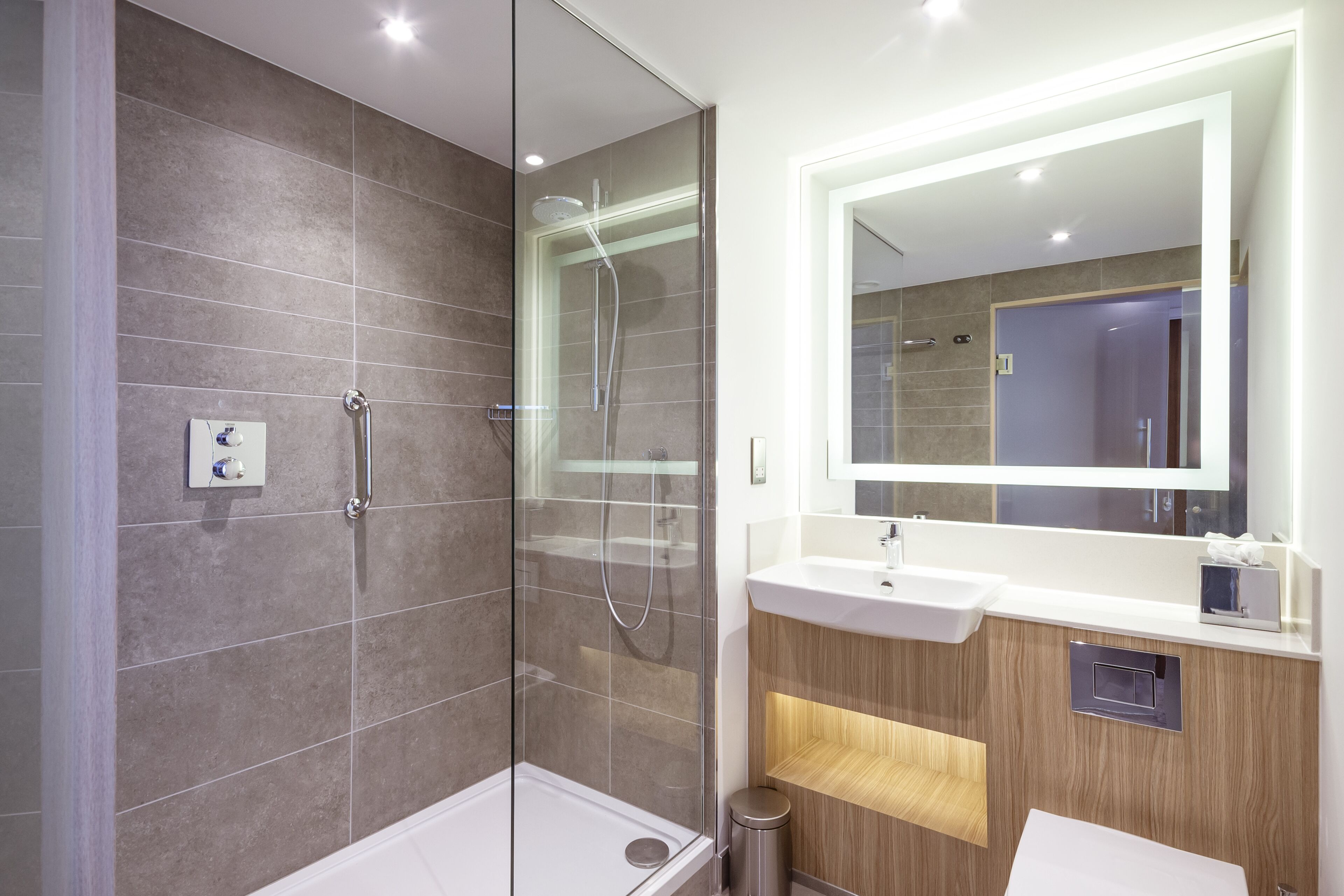 Un ba ño moderno con cabina de ducha de vidrio, tocador con espejo y lavamanos.