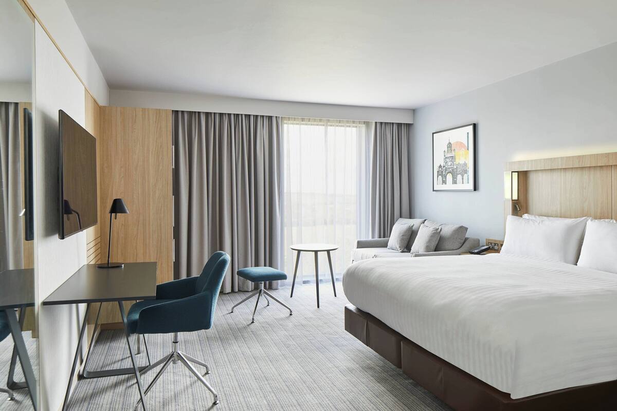 Habitación de hotel con una cama grande, un escritorio con silla, una mesita y un televisor.