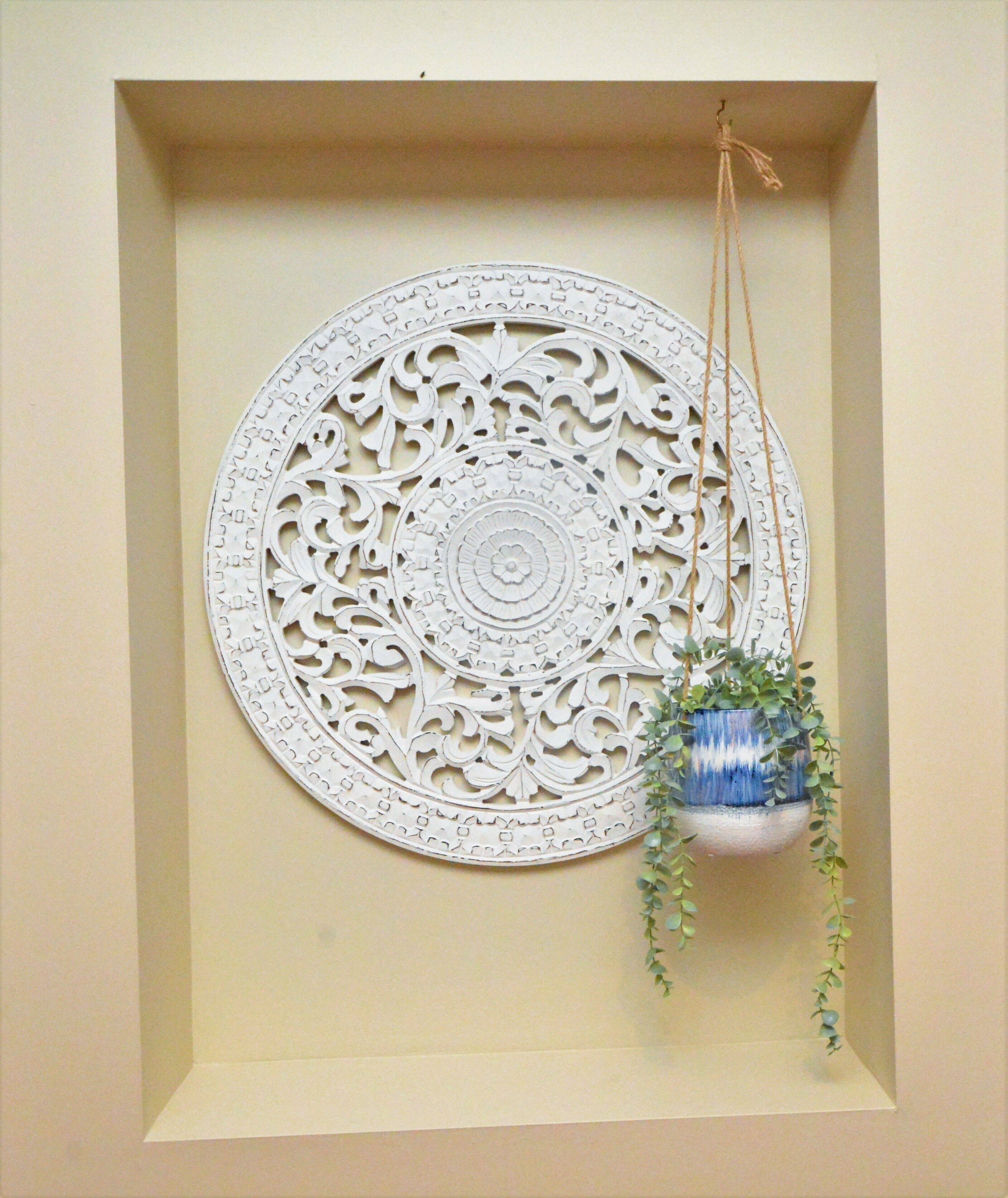 A wall with a circular decorative piece and a hanging planter with greenery.