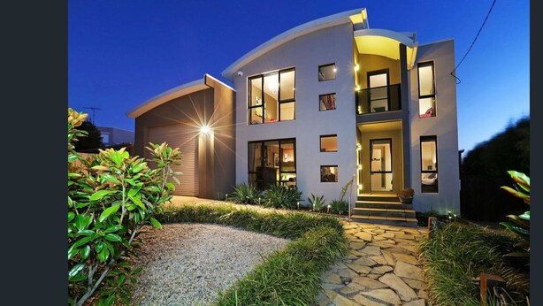 A modern two-story house with a curved facade, multiple windows, and a well-lit entrance. - Castle on the Hill, Ocean Grove. (Ocean Grove)