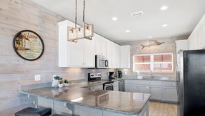 A modern kitchen with a central island, white cabinetry, and a decorative fish skeleton on the wall. - Lagoon Views | Beach Access | Pool and Pier Amenities (Gulf Shores)